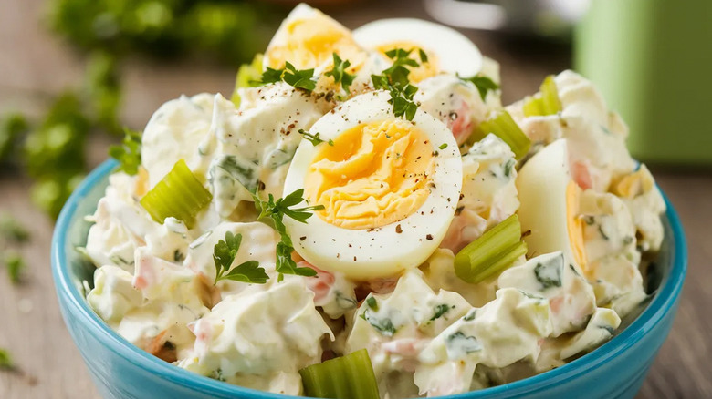 Potato salad with boiled eggs, parsley, and celery in a turquoise bowl