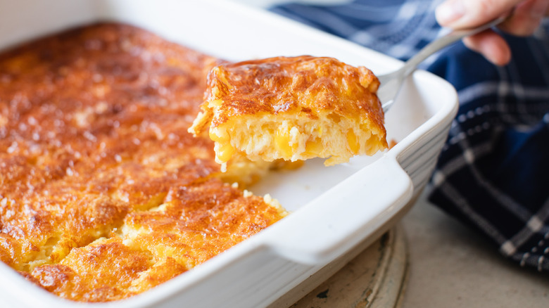 hand holding a forkful of corn casserole over a white baking dish