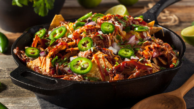 Nachos in an iron skillet with pulled pork, bbq sauce, and jalapenos