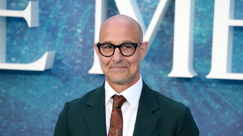 Stanley Tucci, from the shoulders up, in a suit, tie, and glasses