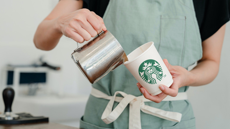A Starbucks barista pours a drink into a paper cup
