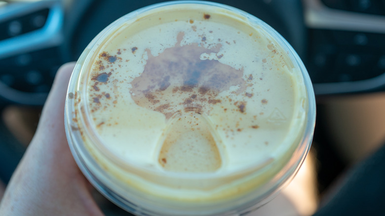 A person seated behind a car steering wheel holds a Starbuck's cold foam beverage