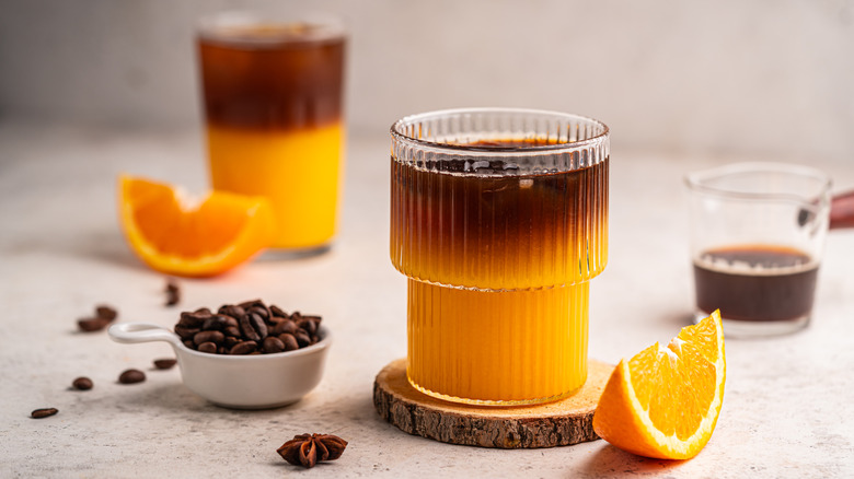 Glasses or orange juice combined with coffee next to slices of oranges and coffee beans