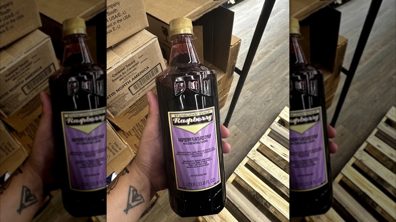 A hand holding a large bottle of raspberry syrup