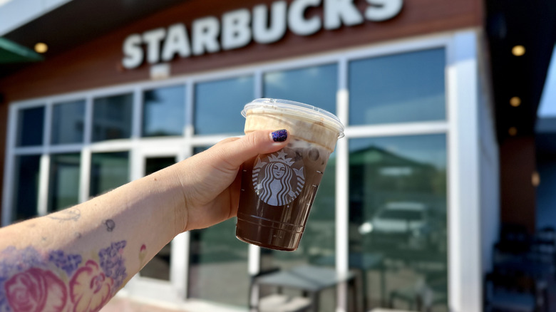 Holding an Iced Dubai Chocolate Mocha in front of Starbucks sign