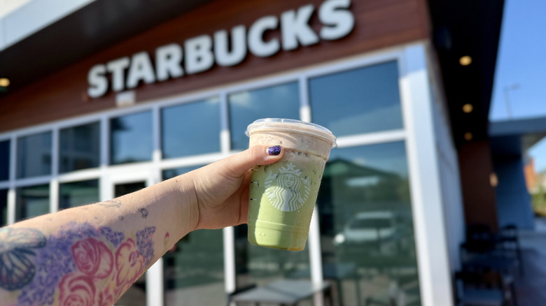 Arm holding an Iced Dubai Chocolate Matcha in front of Starbucks