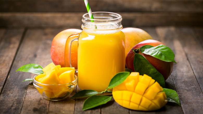 Mango juice in a glass jar with sliced mangos and whole mangos