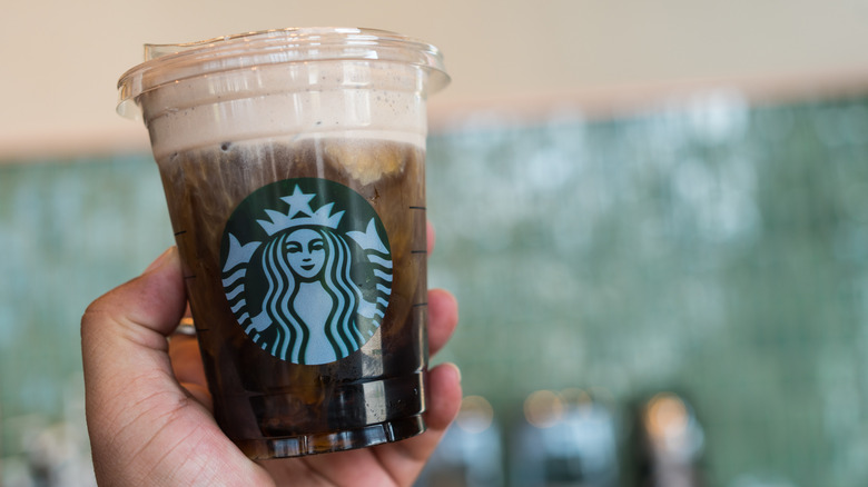 A person holding an iced coffee with cold foam on top of it
