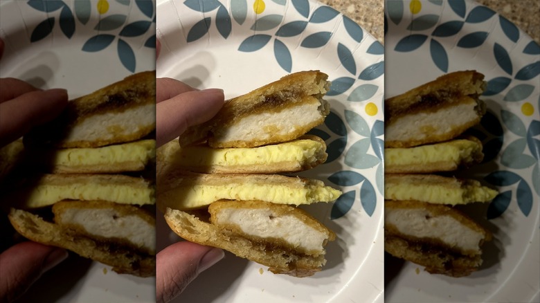 Hand holding chicken, maple butter, and egg breakfast sandwich