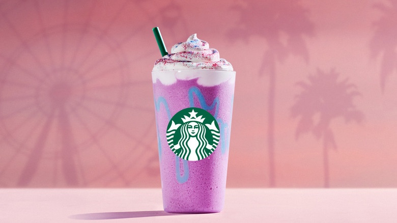 A Unicorn Frappuccino against a pink background with the outline of a Ferris wheel and palm trees on it.