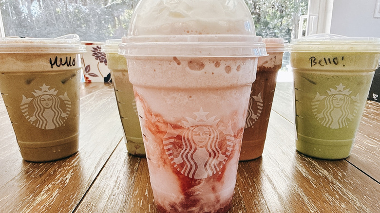 Five Starbucks Valentine's drinks with the Strawberry Shortcake Frappuccino front and center on a wooden table