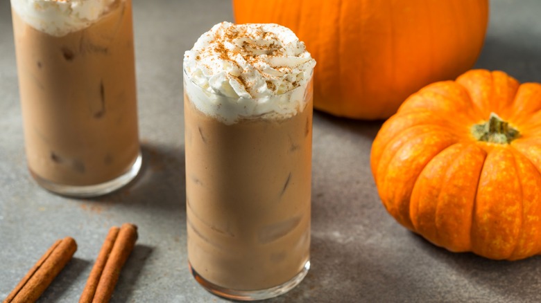 Pumpkin spice lattes in glasses next to pumpkins and cinnamon sticks