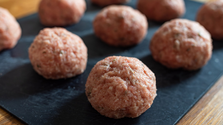 Raw meatballs on black board on wooden table.