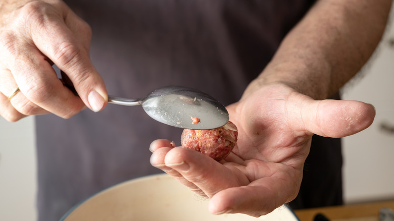 Hands of a man forming balls of raw minced meat with a spoon to make meatballs.