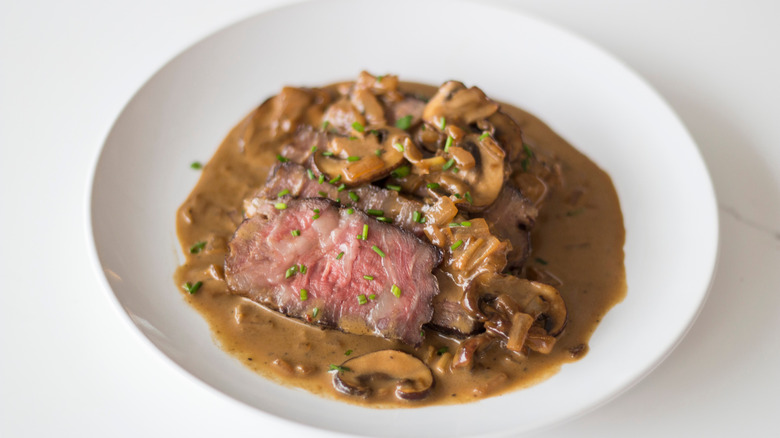 A white plate with steak Diane (featuring sliced pieces of steak) on it.