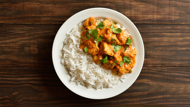 Butter chicken in a white bowl with cilantro leaves and rice