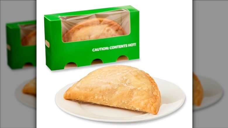Two Freshness Guaranteed Caramel Apple Empanadas, one in a green cardboard bakery box and the other on a white plate, on a white background