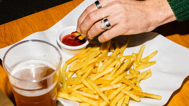 Hand dipping french fries in ketchup