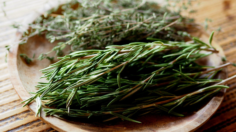 Sprigs of rosemary on a wooden plate, placed on a wood table