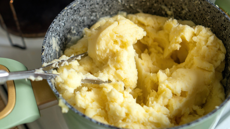 Freshly mashed potatoes in a grey bowl with a light green handle