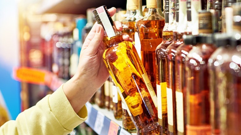 Hand pulling a whiskey bottle from a store shelf.