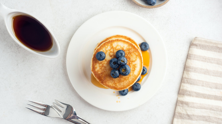 A plate with blueberry pancakes and a dish of syrup next to it