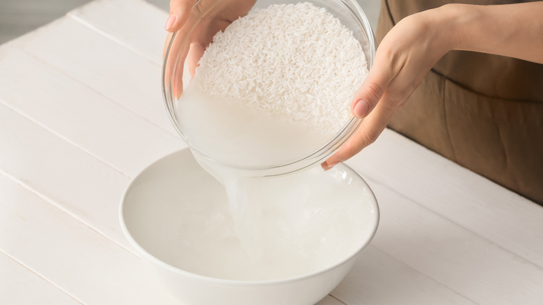 Hands pouring water from washed rice into bowl