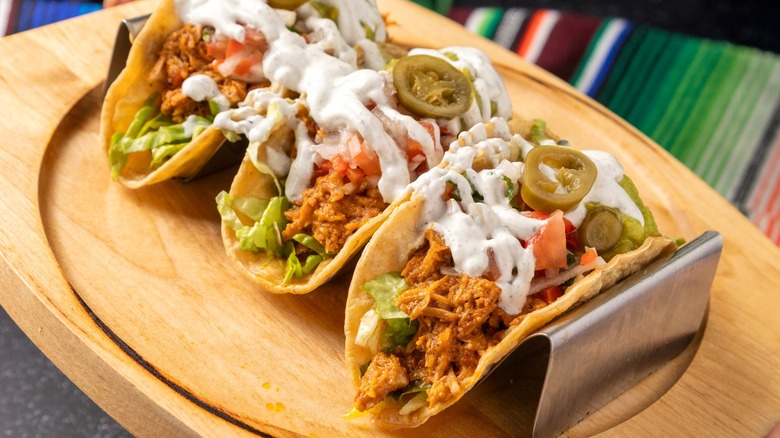 Person holding wooden tray with three tacos