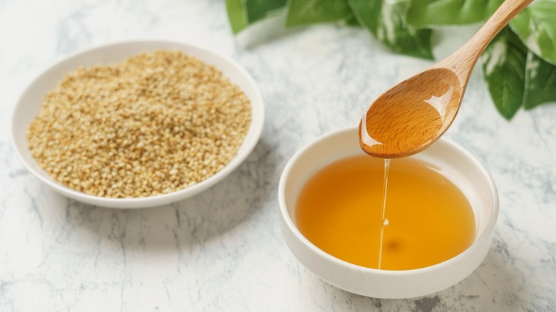 Sesame oil with wooden spoon and sesame seeds in white bowls