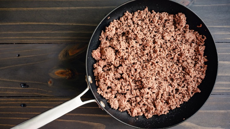 Ground beef in a large frying pan sitting on a wooden table