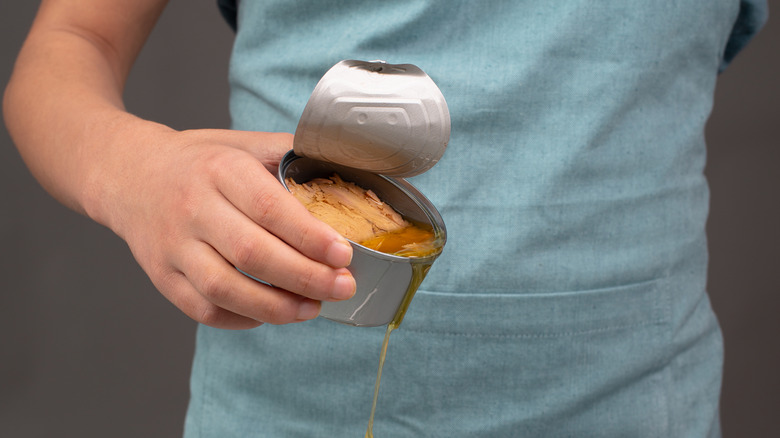 Hand pouring oil from can of tuna 