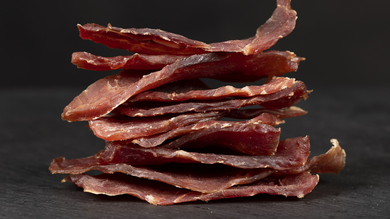 Thin pieces of beef jerky piled on top of one another in front of a black background