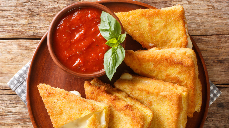 Mozzarella in carrozza on a wood plate with marinara dipping sauce and basil leaves