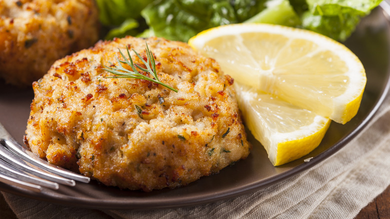 A fish cake on a plate with two slices of lemon.