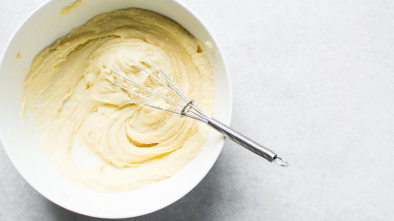 A top-down view of butter being mixed into sugar in a white bowl