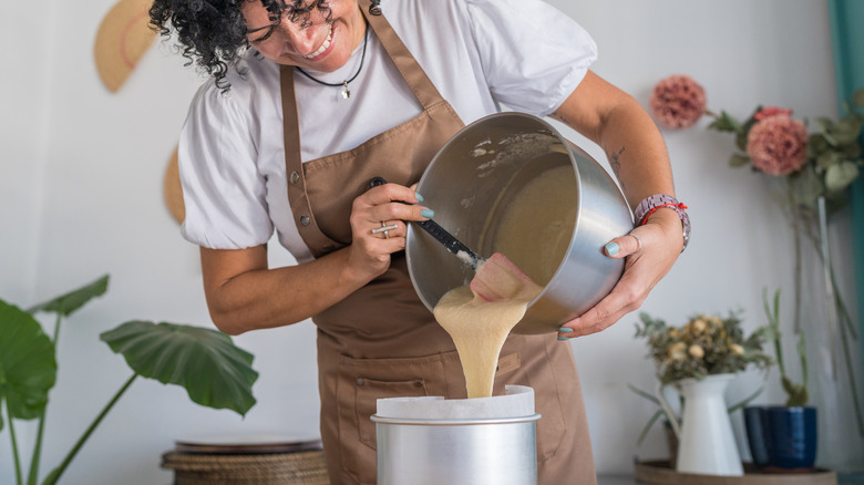 A person pouring cake batter out of a mixing bowl into a tin.