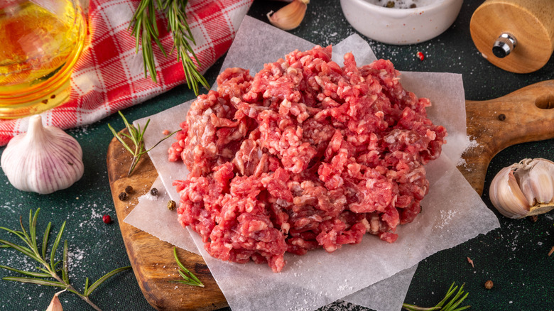 Raw ground beef with rosemary, garlic, and other aromatics nearby