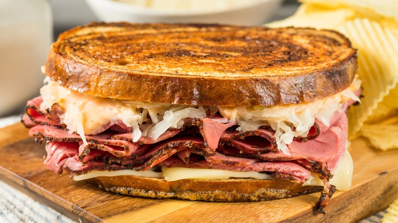 Reuben sandwich layered with Swiss cheese, corned beef, and sauerkraut on a wood board