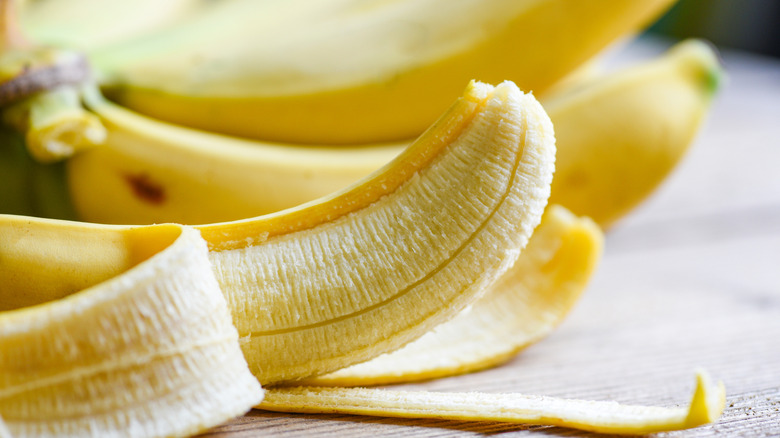 Partly peeled banana lying on its side on a light wooden surface with others bananas in the background