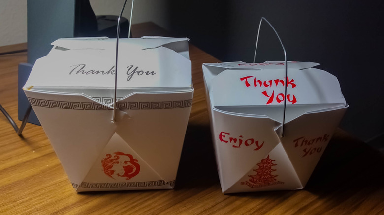 two closed Chinese food takeout containers sitting on a wooden table