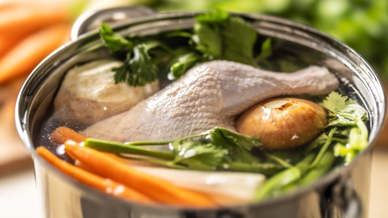 Chicken stock with poultry and vegetables simmering in a large metal pot