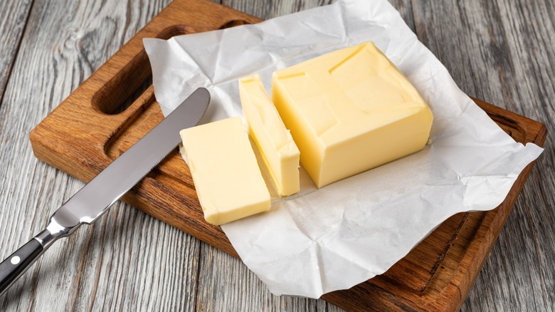 Fresh butter slices on a wooden cutting board with a butter knife, ready for spreading