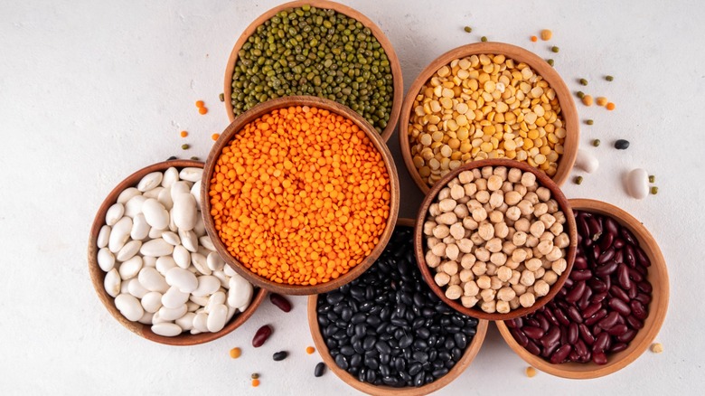 Various dried beans, lentils, mung, chickpea, pea assortment in wooden bowls. Legumes on white table top view. Vegan protein sources food, copy space