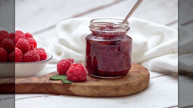 Jar of raspberry jam on wooden board with raspberries