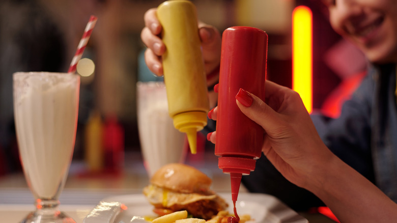 Hands squeezing mustard and ketchup onto burgers