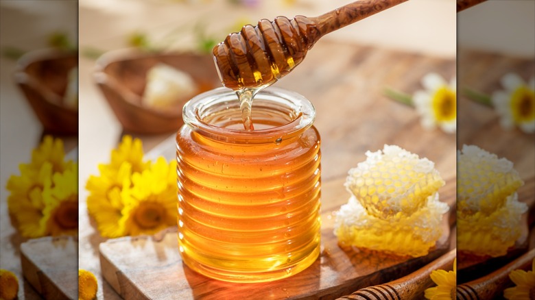 Natural organic honey in glass jar, honey dipper and honeycombs are near