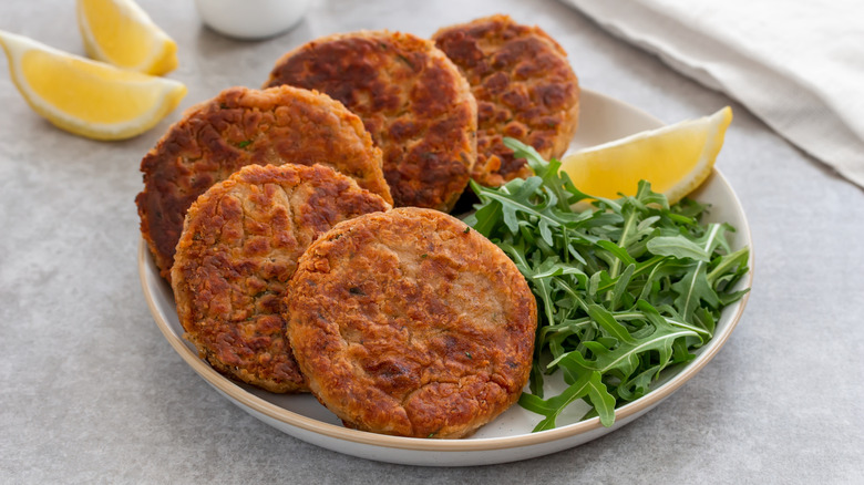 Cooked tuna patties in a white dish with arugula and lemon wedges