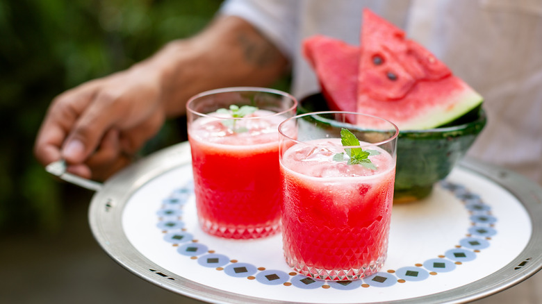 Person holding tray of watermelon slices and two drinks.