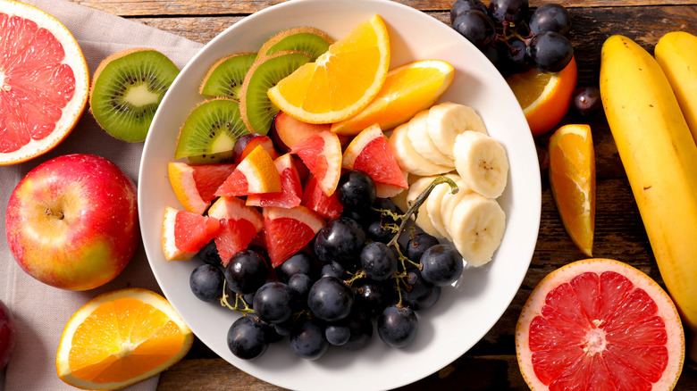 Colorful fruit salad on a white dish surrounded by whole fruits