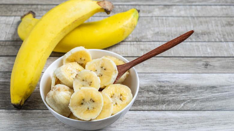 Two whole bananas and a bowl of sliced bananas on a table